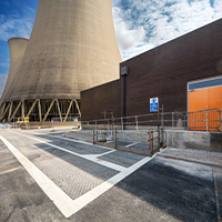 Cooling towers with a clear sky above, adjacent to an industrial building. A blue handicap sign and an orange door are visible, creating an industrial tone.