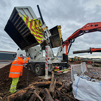 Construction site with workers in high-visibility clothing operating heavy machinery. Truck unloading soil near excavator under cloudy skies.